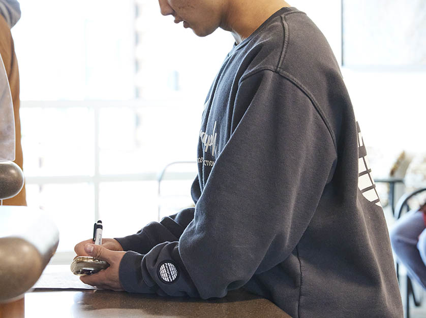 Male student looks down at hand held device and writes notes on it.