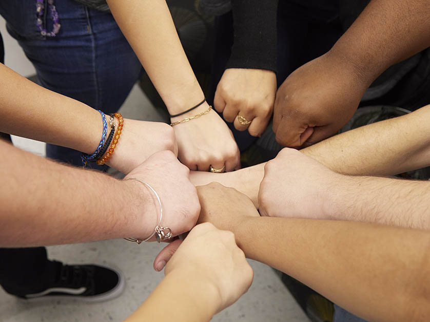 Close-up overview of the formation made of nine students' fists touching in the center in a team exercise.